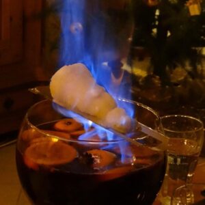 Flaming sugar cone over a bowl of Feuerzangenbowle with fruit slices.