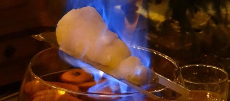 Flaming sugar cone over a bowl of Feuerzangenbowle with fruit slices.