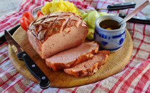 Traditional German meal with roasted pork, tomatoes, and a knife on a wooden board.