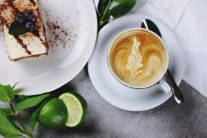 A cup of coffee and a slice of cake on a plate, set on a wooden table.