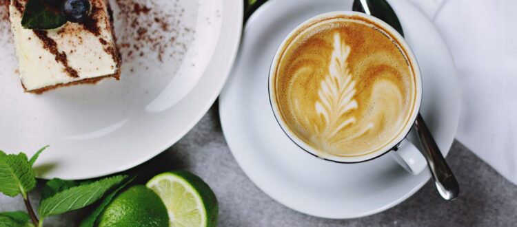 A cup of coffee and a slice of cake on a plate, set on a wooden table.