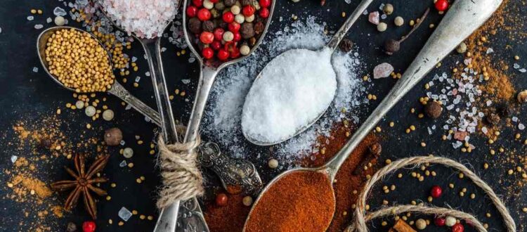 Various spices and seasonings in spoons on a dark background.