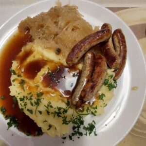 A plate of mashed potatoes with gravy, Nuremberg sausages, and sauerkraut.