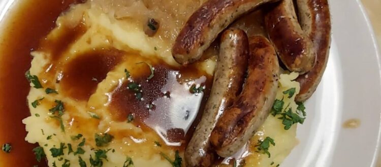 A plate of mashed potatoes with gravy, Nuremberg sausages, and sauerkraut.