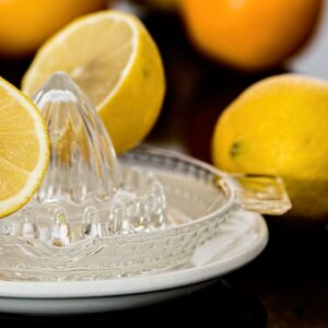 A glass lemon squeezer with a halved lemon and whole lemons around it.