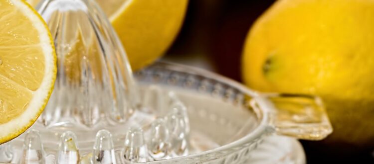 A glass lemon squeezer with a halved lemon and whole lemons around it.