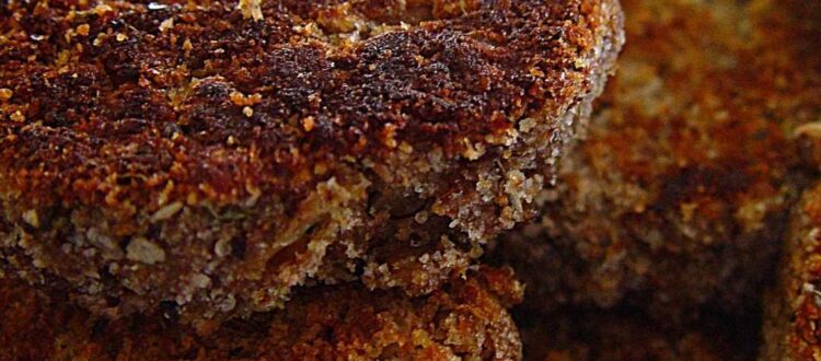 Close-up of freshly fried Berliner Buletten with a golden-brown crust, served on a plate with mustard and fresh parsley.