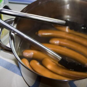 Bockwurst sausages simmering in hot water with tongs resting on the pot’s edge, illustrating how to cook Bockwurst correctly.