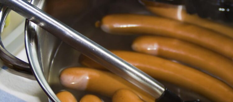 Bockwurst sausages simmering in hot water with tongs resting on the pot’s edge, illustrating how to cook Bockwurst correctly.