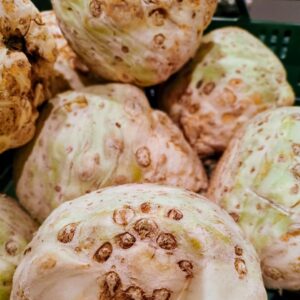 A close-up image of freshly harvested celeriac roots with distinctive rough, knobby textures arranged in a green crate.