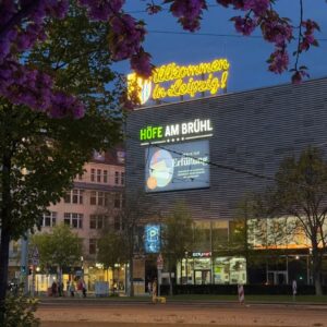 Neon sign "Willkommen in Leipzig" above Höfe am Brühl shopping center at dusk